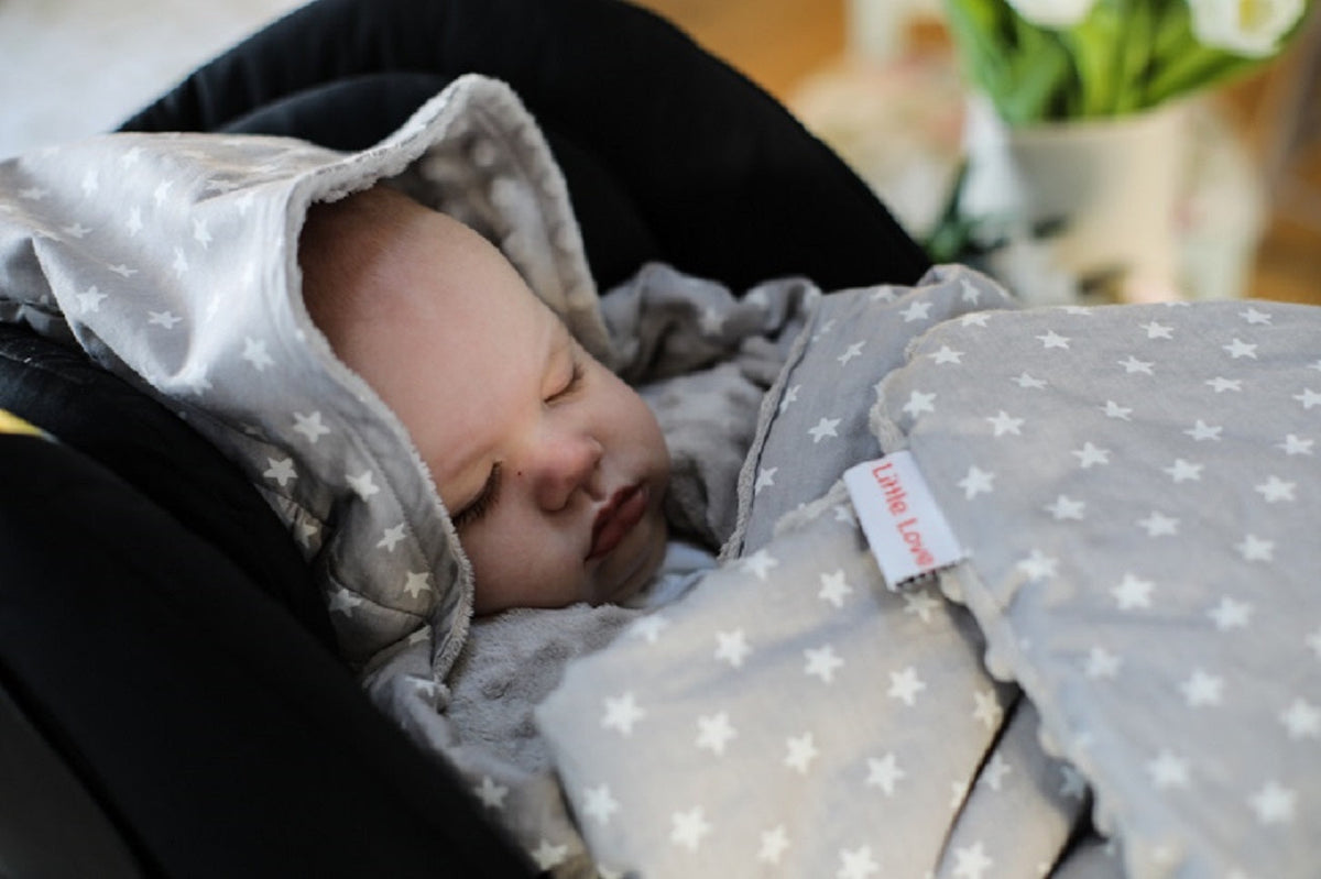 Newborn baby asleep in an infant car seat, wrapped in a grey star Little Love blanket