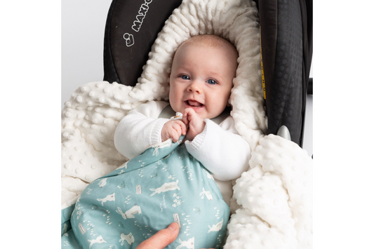 Baby smiling in an infant car seat under a Teal Bunnies car seat blanket
